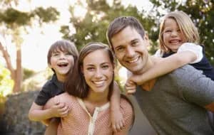 Família somrient a l'aire lliure, pares amb els seus dos fills a coll