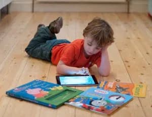 child lying down with an ipad and books on the floor